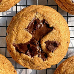 A cookie with chocolate chunks sits on a cooling rack. Shop online for the best eggless cookies in India: Mumbai, Bangalore, Delhi.
