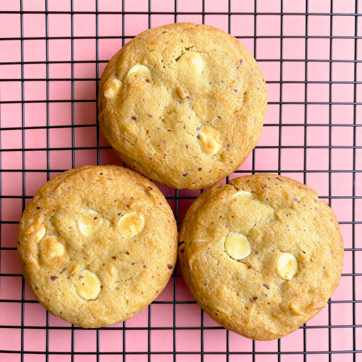 Three Biscoff White Choco Chip Cookies on a cooling rack, showing their golden-brown texture and melted white chocolate chips