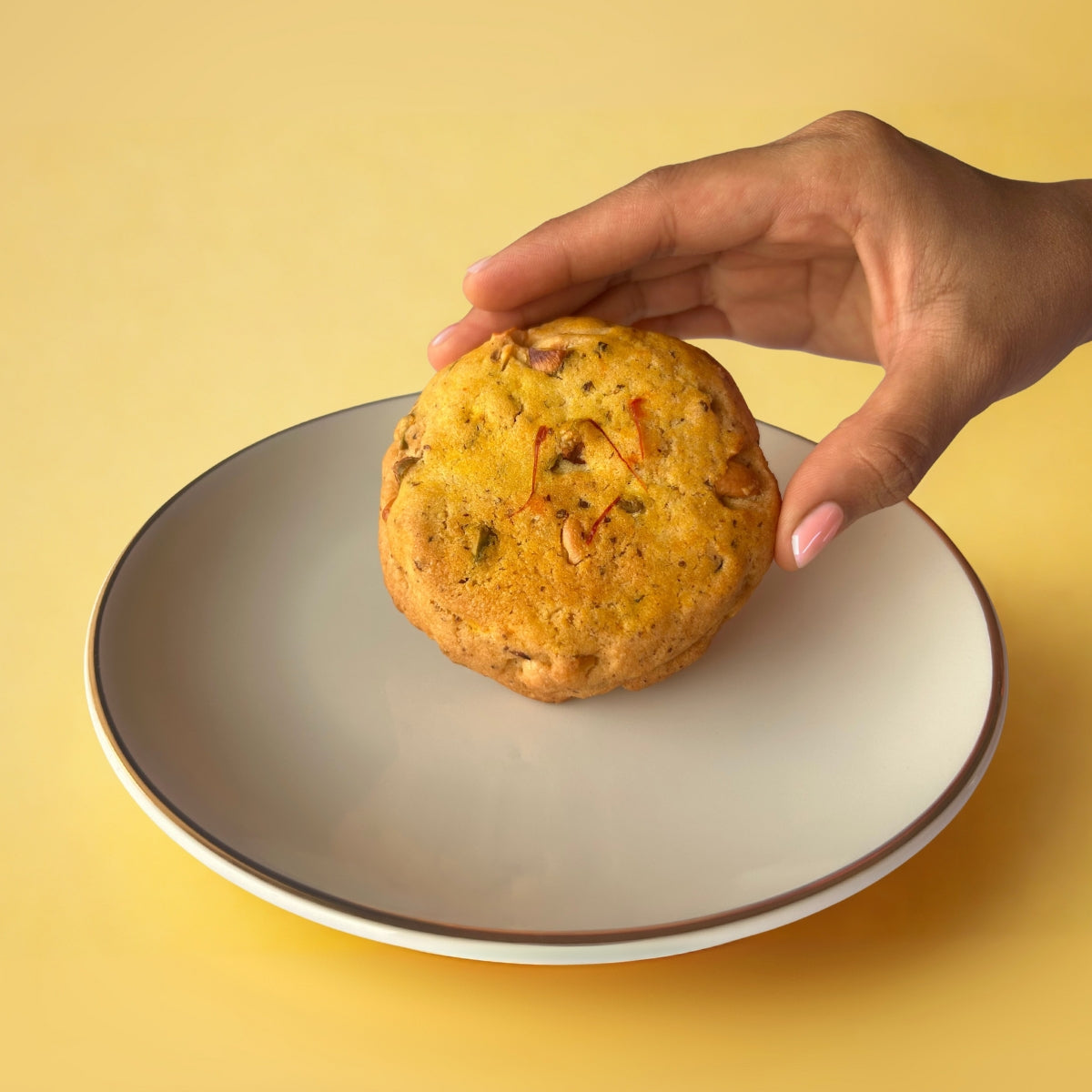 Hand holding Kesar Pista Cookie with saffron and pistachios, premium eggless dry fruit cookie to buy online in India from Queen Cookies
